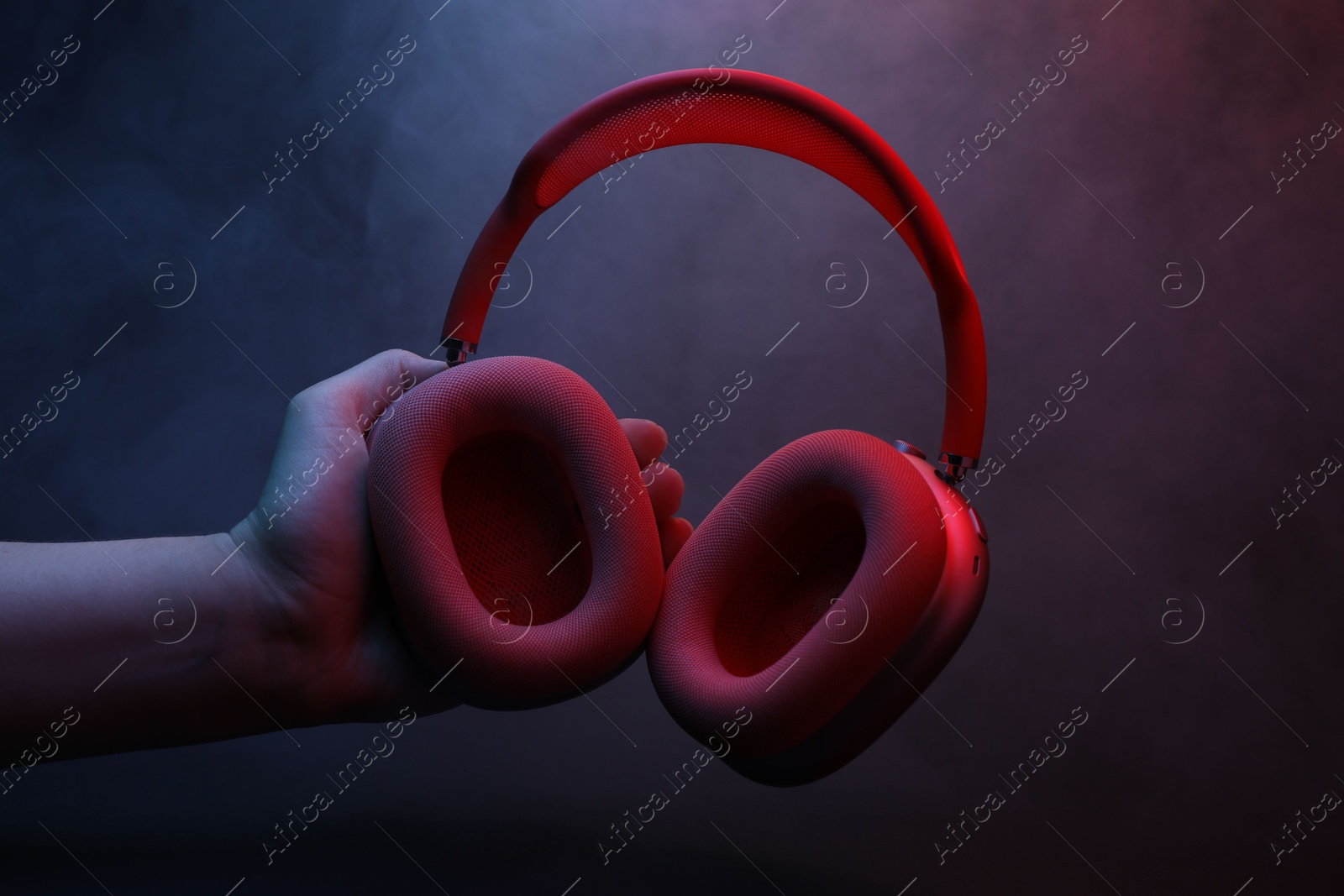 Woman holding wireless headphones on dark background with color lights and smoke, closeup Photo of Woman holding wireless headphones on dark background with color lights and smoke, closeup