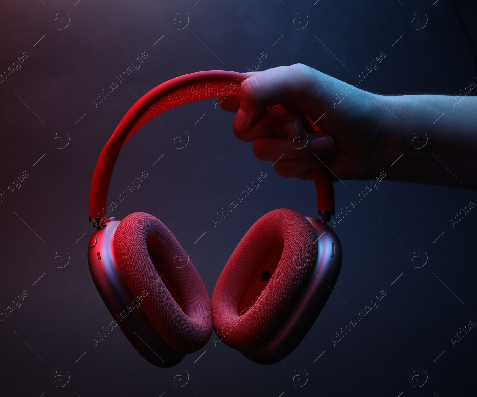Woman holding wireless headphones on dark background with color lights and smoke, closeup Photo of Woman holding wireless headphones on dark background with color lights and smoke, closeup