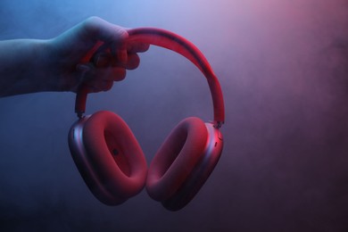 Photo of Woman holding wireless headphones on dark background with color lights and smoke, closeup