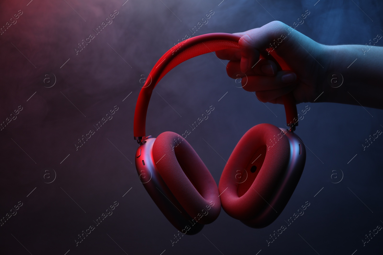 Woman holding wireless headphones on dark background with color lights and smoke, closeup Photo of Woman holding wireless headphones on dark background with color lights and smoke, closeup