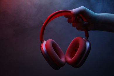Photo of Woman holding wireless headphones on dark background with color lights and smoke, closeup