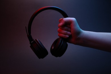 Photo of Woman holding wireless headphones on dark background, closeup