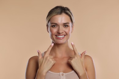 Photo of Woman pointing at her healthy teeth on beige background