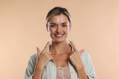 Photo of Woman pointing at her healthy teeth on beige background