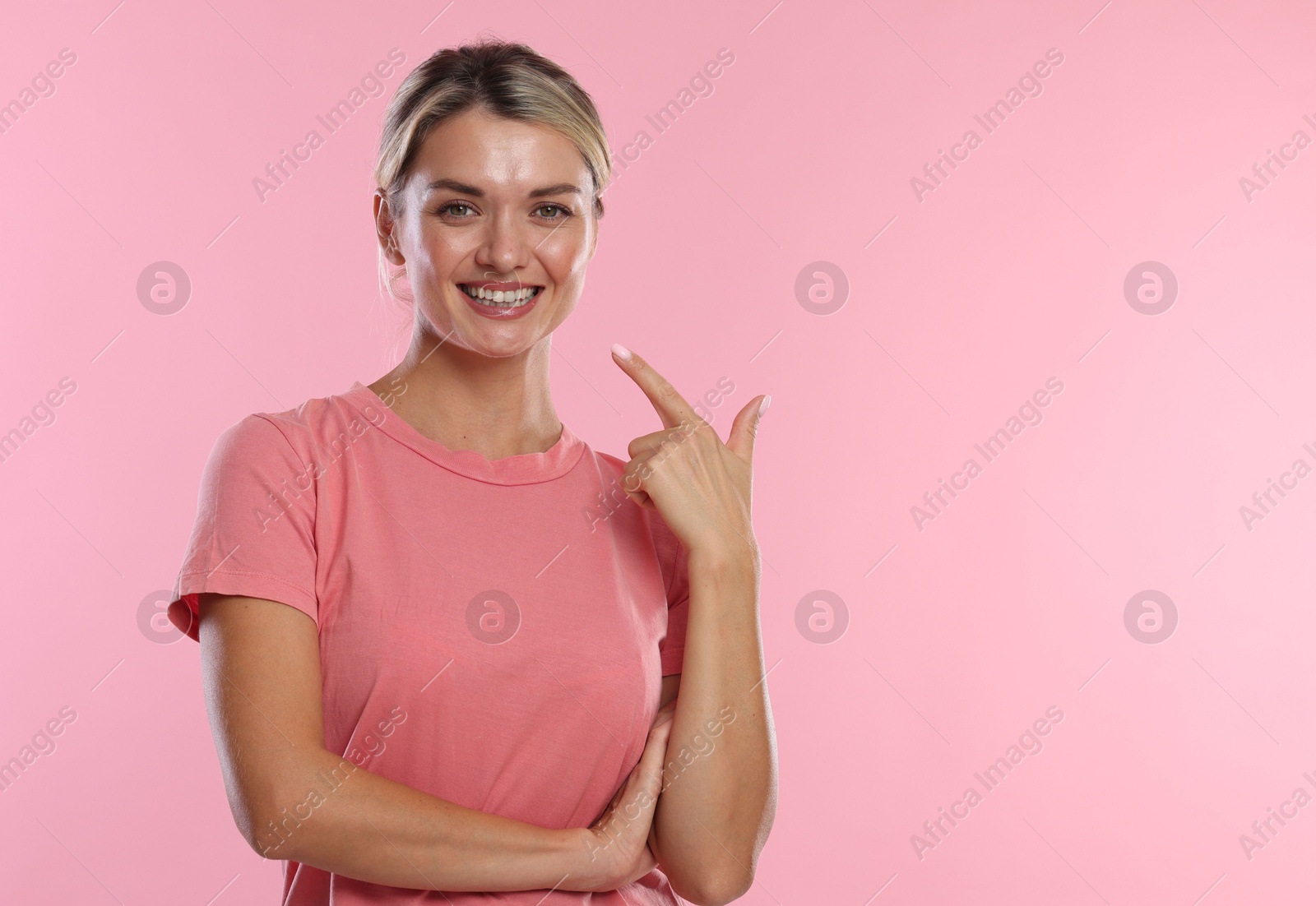 Photo of Woman pointing at her healthy teeth on pink background. Space for text