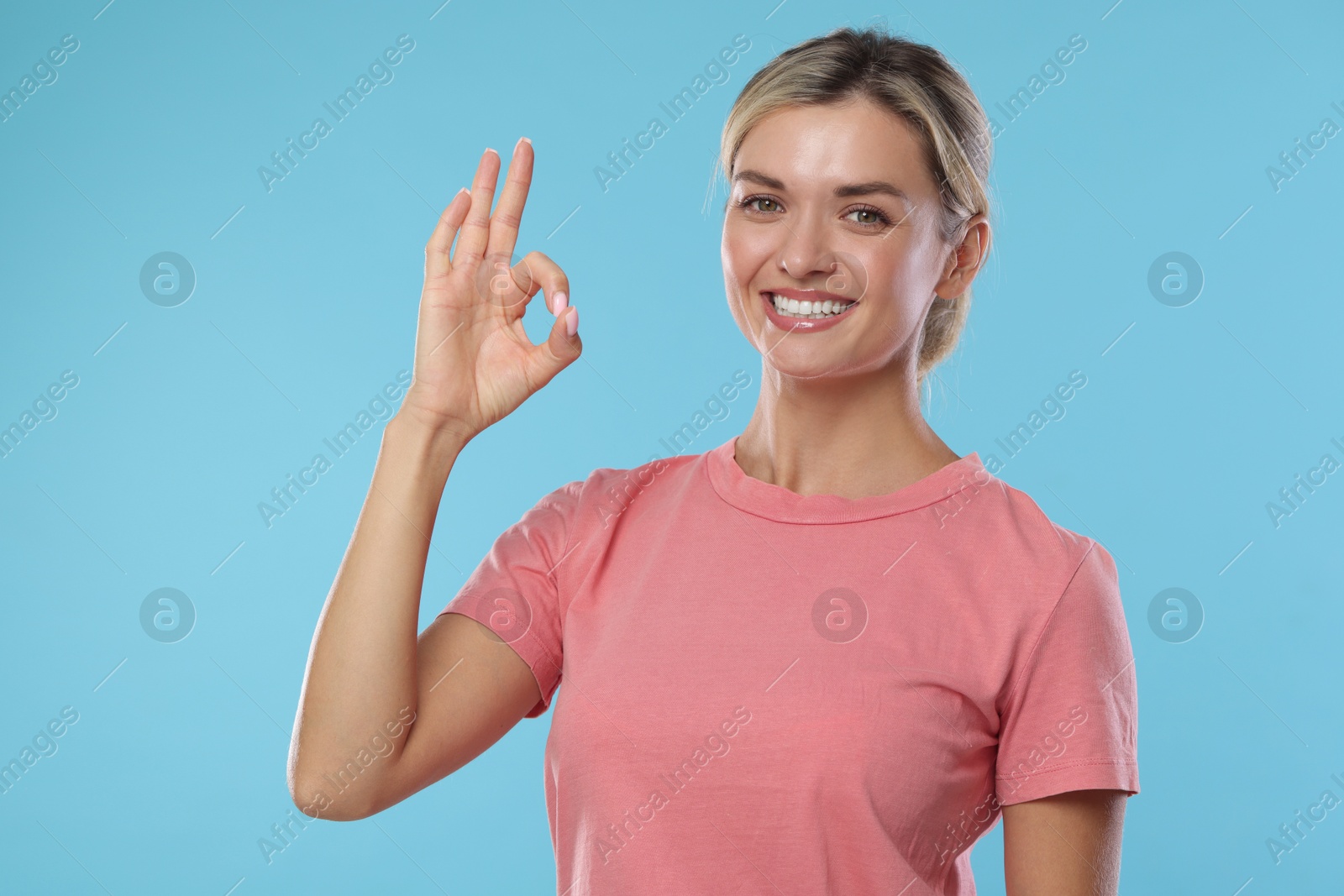 Photo of Woman with perfect healthy teeth showing okay gesture on light blue background