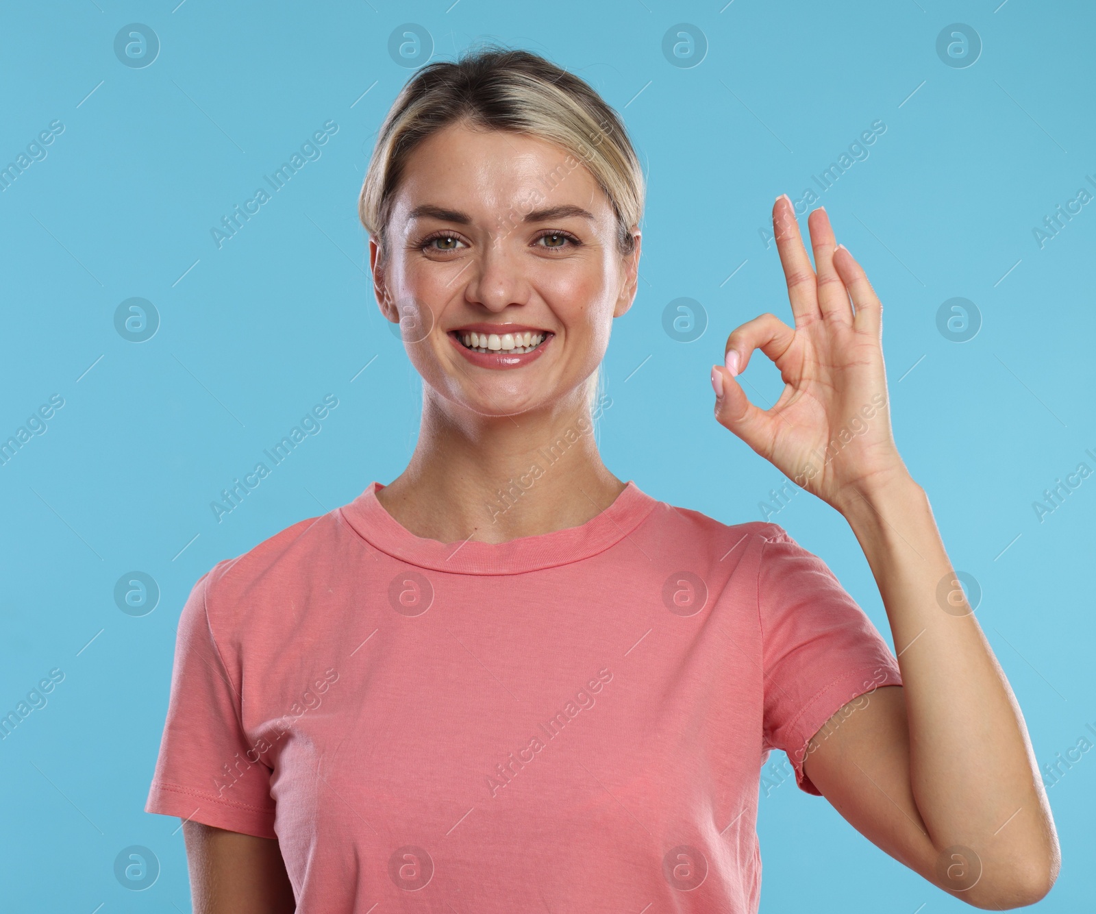 Photo of Woman with perfect healthy teeth showing okay gesture on light blue background