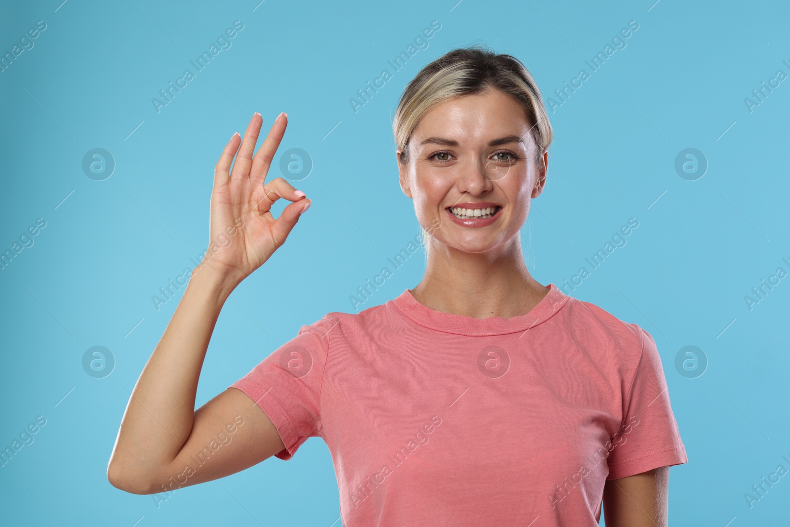 Photo of Woman with perfect healthy teeth showing okay gesture on light blue background