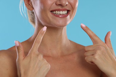 Photo of Woman pointing at her healthy teeth on light blue background, closeup