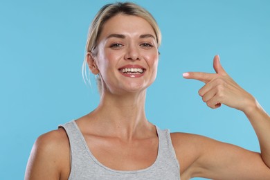 Photo of Woman pointing at her healthy teeth on light blue background