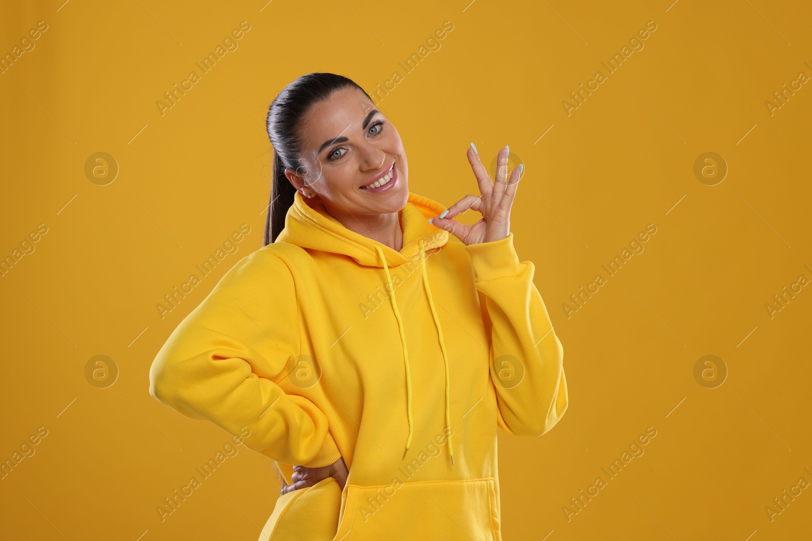 Photo of Woman with perfect healthy teeth showing okay gesture on yellow background