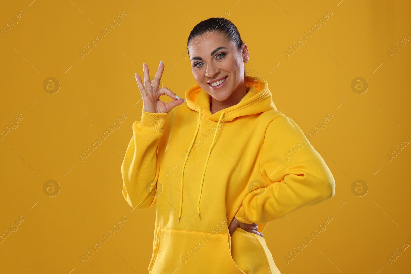 Photo of Woman with perfect healthy teeth showing okay gesture on yellow background