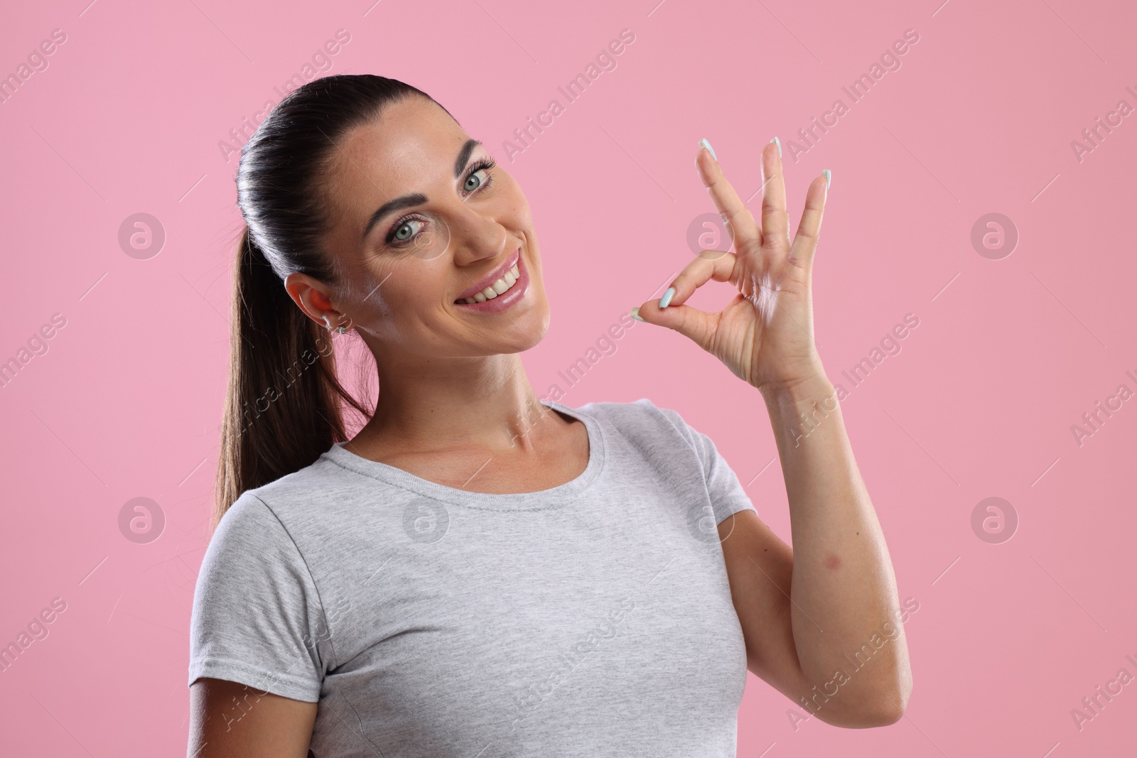 Photo of Woman with perfect healthy teeth showing okay gesture on pink background