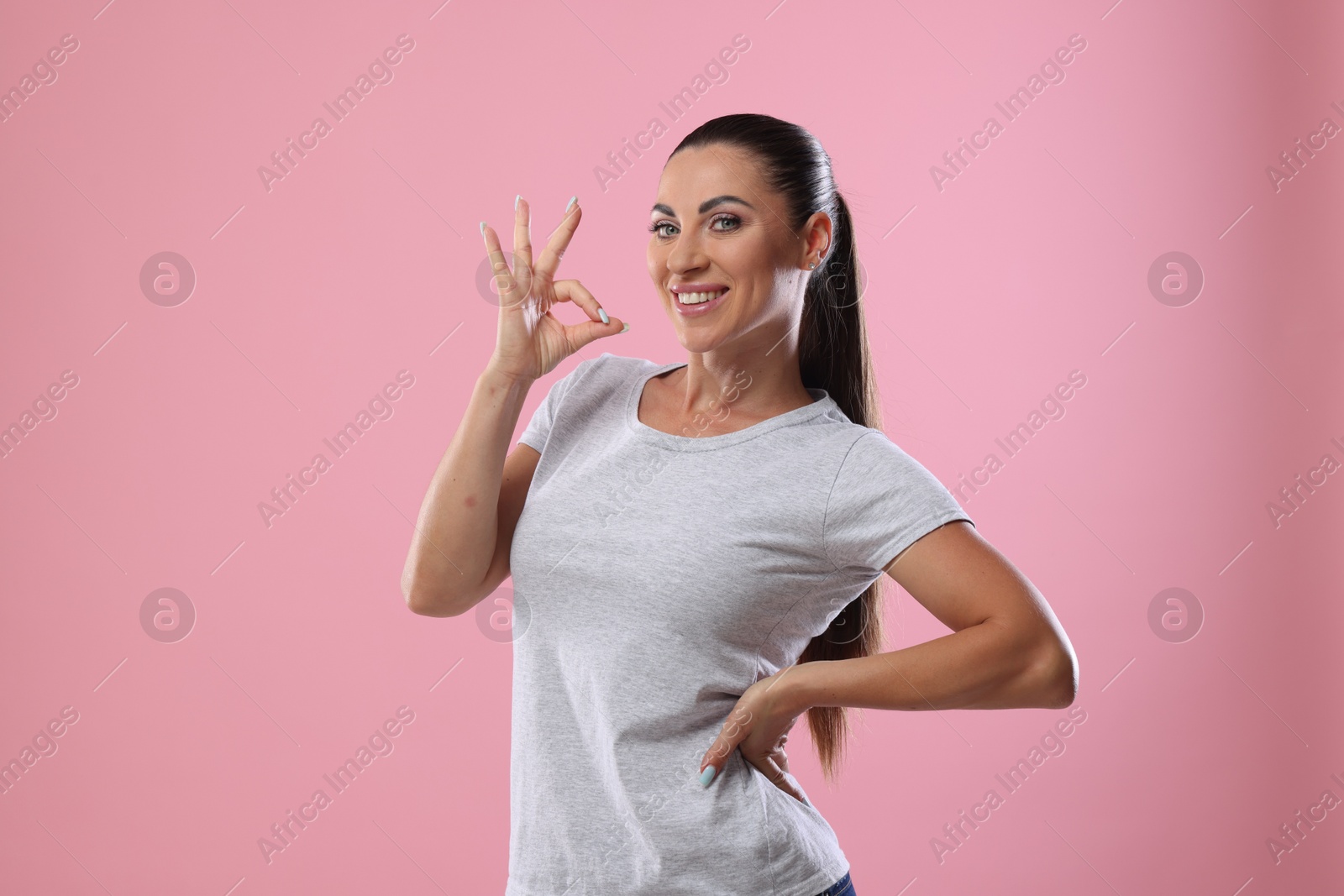 Photo of Woman with perfect healthy teeth showing okay gesture on pink background