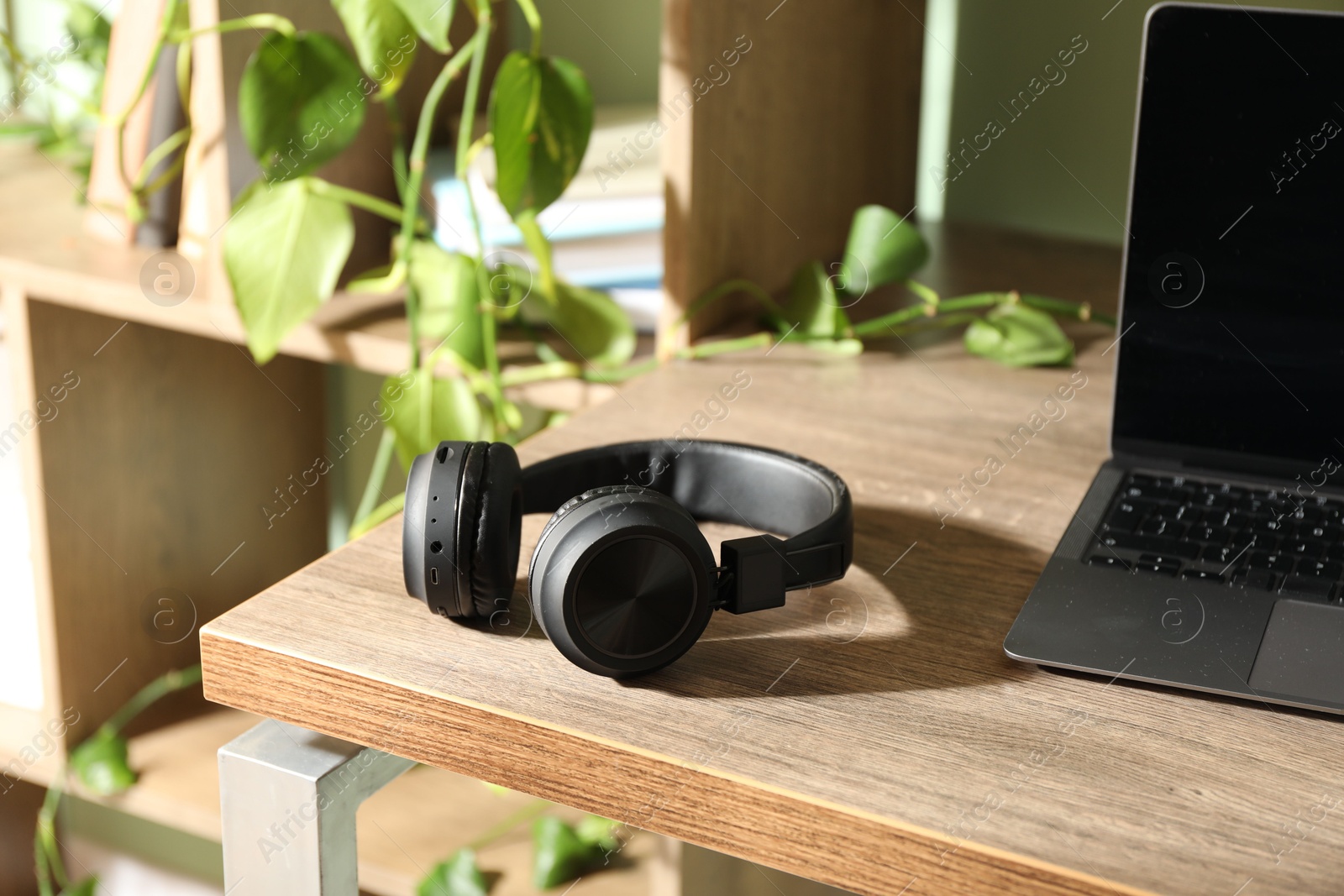 Laptop and wireless headphones on wooden table indoors Photo of Laptop and wireless headphones on wooden table indoors