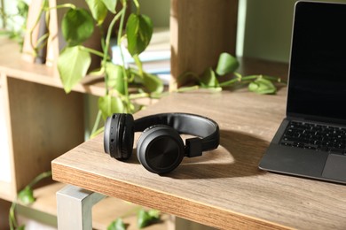 Photo of Laptop and wireless headphones on wooden table indoors