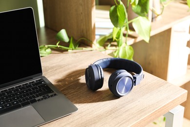 Photo of Laptop and wireless headphones on wooden table indoors