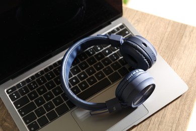 Photo of Laptop and wireless headphones on wooden table indoors, closeup