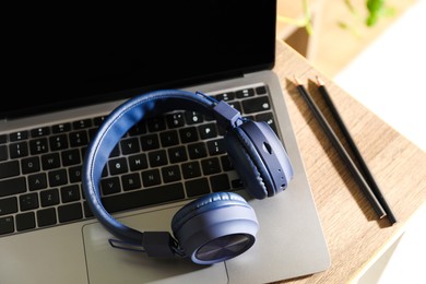 Photo of Laptop, wireless headphones and pencils on wooden table indoors, closeup