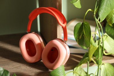 Photo of Wireless headphones and houseplant on wooden table indoors, closeup