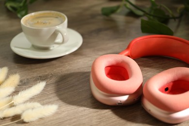 Photo of Wireless headphones, cup of coffee and spikes on wooden table indoors, closeup