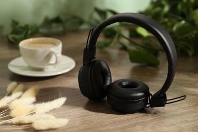 Photo of Wireless headphones, cup of coffee and spikes on wooden table indoors, closeup