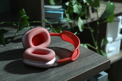 Photo of Wireless headphones and houseplant on black wooden table indoors, closeup
