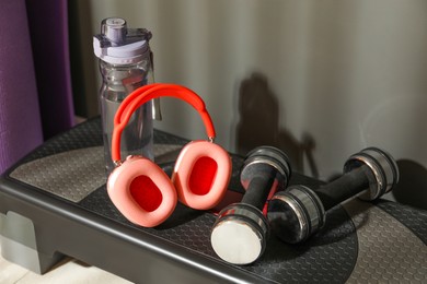 Photo of Wireless headphones, bottle of water and dumbbells on step platform in gym