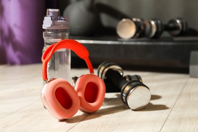 Photo of Wireless headphones, bottle of water and dumbbells on floor in gym