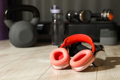 Photo of Wireless headphones and dumbbells on floor in gym. Space for text