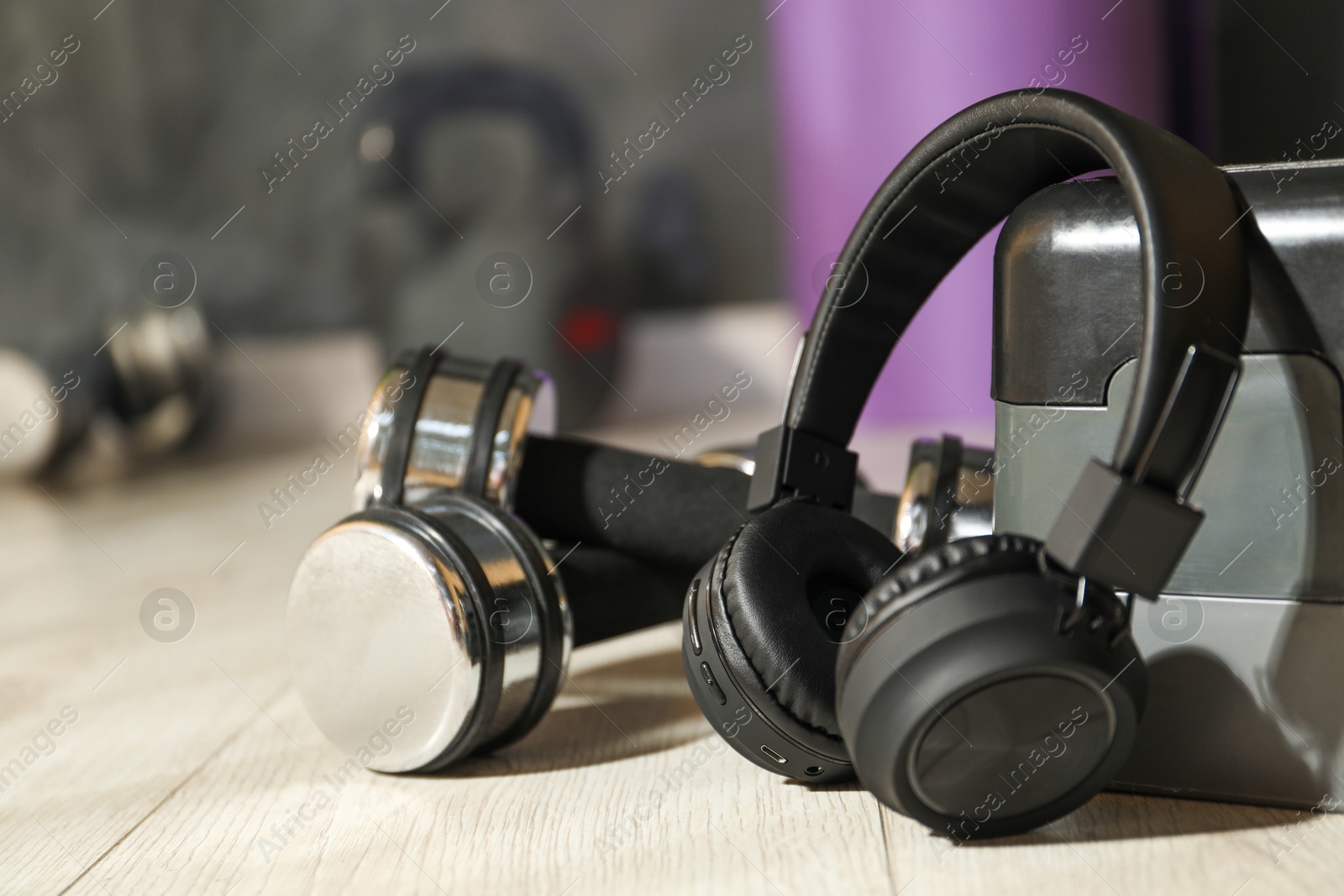 Wireless headphones, dumbbells and step platform on floor in gym, closeup Photo of Wireless headphones, dumbbells and step platform on floor in gym, closeup