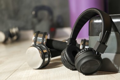 Photo of Wireless headphones, dumbbells and step platform on floor in gym, closeup