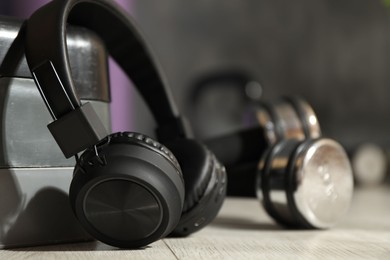 Photo of Wireless headphones, dumbbells and step platform on floor in gym, closeup