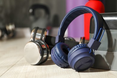 Photo of Wireless headphones, step platform, dumbbells and bottle of water on floor in gym, closeup