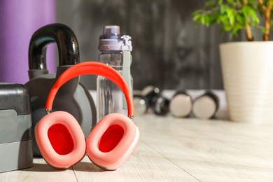 Photo of Wireless headphones, step platform, kettlebell and bottle of water on floor in gym, closeup. Space for text