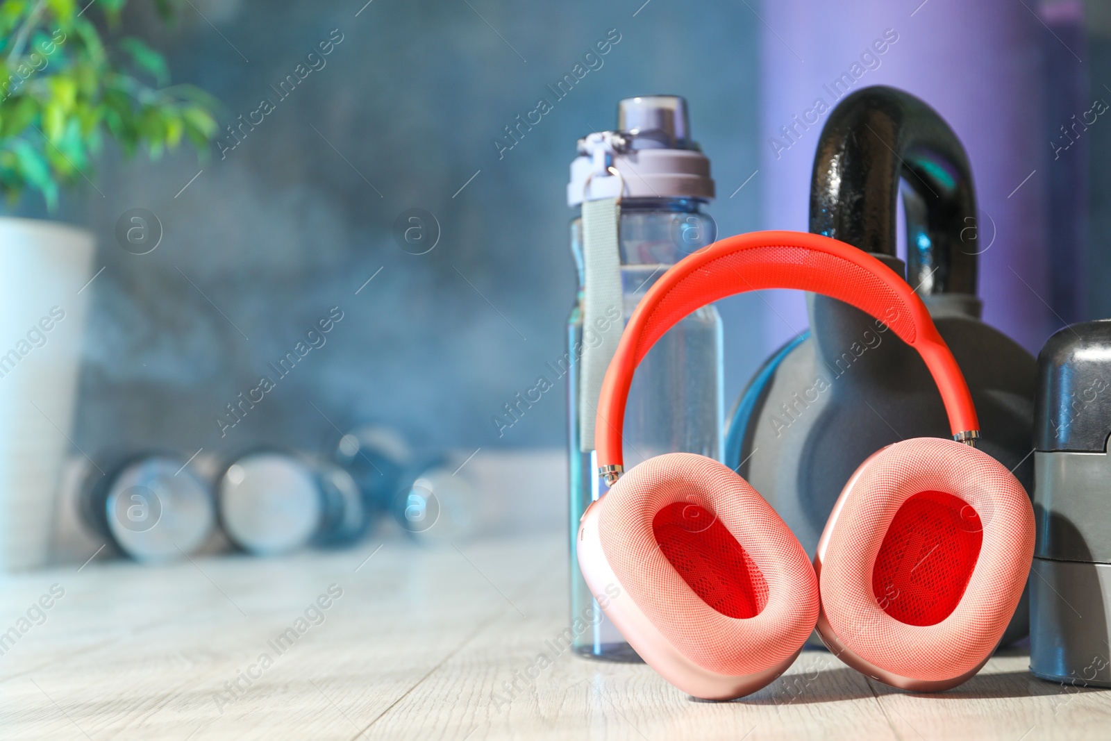 Wireless headphones, kettlebell and bottle of water on floor in gym, closeup. Space for text Photo of Wireless headphones, kettlebell and bottle of water on floor in gym, closeup. Space for text