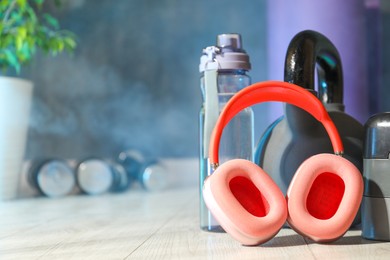 Photo of Wireless headphones, kettlebell and bottle of water on floor in gym, closeup. Space for text
