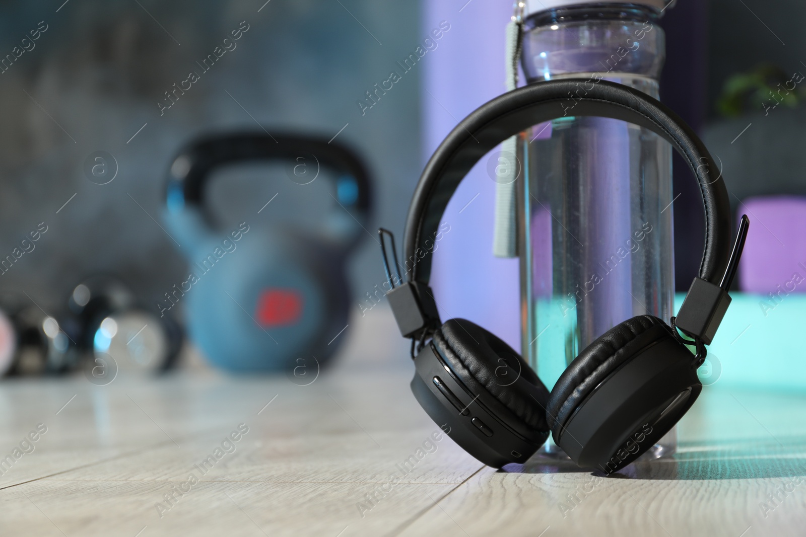 Wireless headphones and bottle of water on floor in gym, closeup. Space for text Photo of Wireless headphones and bottle of water on floor in gym, closeup. Space for text