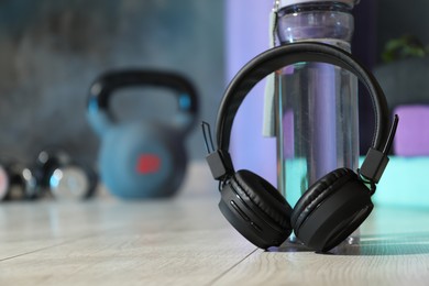 Photo of Wireless headphones and bottle of water on floor in gym, closeup. Space for text
