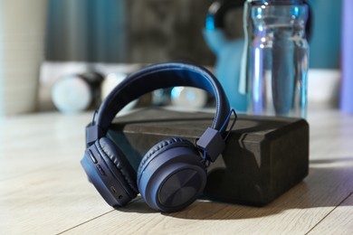 Photo of Wireless headphones, yoga block and bottle of water on floor in gym, closeup