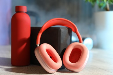 Photo of Wireless headphones, yoga block and bottle of water on floor in gym, closeup