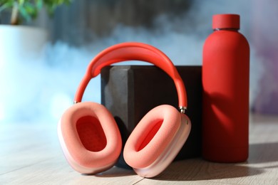 Photo of Wireless headphones, yoga block and bottle of water on floor in gym, closeup