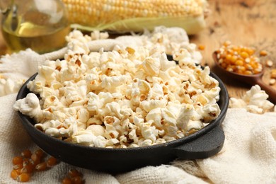 Photo of Tasty popcorn, corn kernels, oil and towel on wooden table, closeup