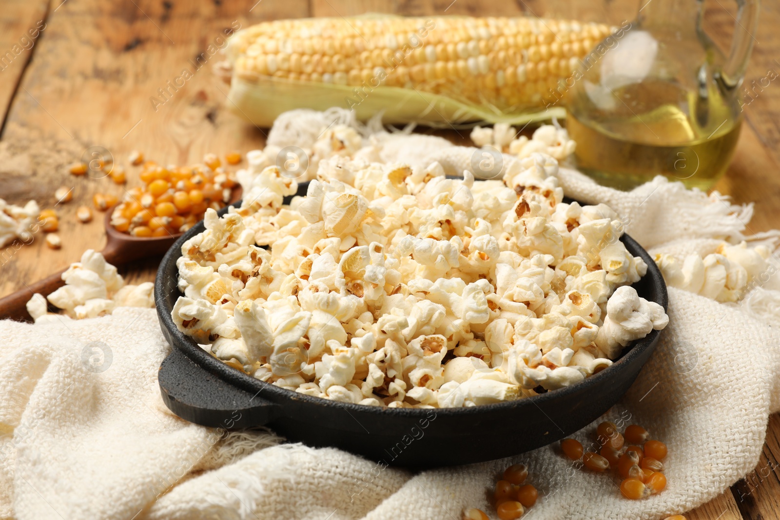 Photo of Tasty popcorn, corn kernels, oil and towel on wooden table, closeup