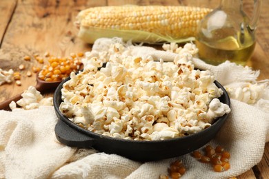 Photo of Tasty popcorn, corn kernels, oil and towel on wooden table, closeup