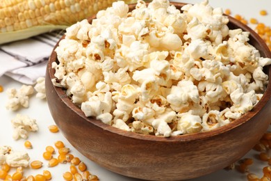Photo of Tasty popcorn and corn kernels on white table, closeup