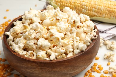 Photo of Tasty popcorn and corn kernels on white table, closeup