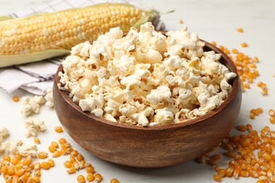 Photo of Tasty popcorn and corn kernels on white table, closeup