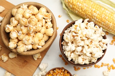 Photo of Tasty popcorn and corn kernels on white table, flat lay