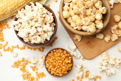 Photo of Tasty popcorn and corn kernels on white table, flat lay